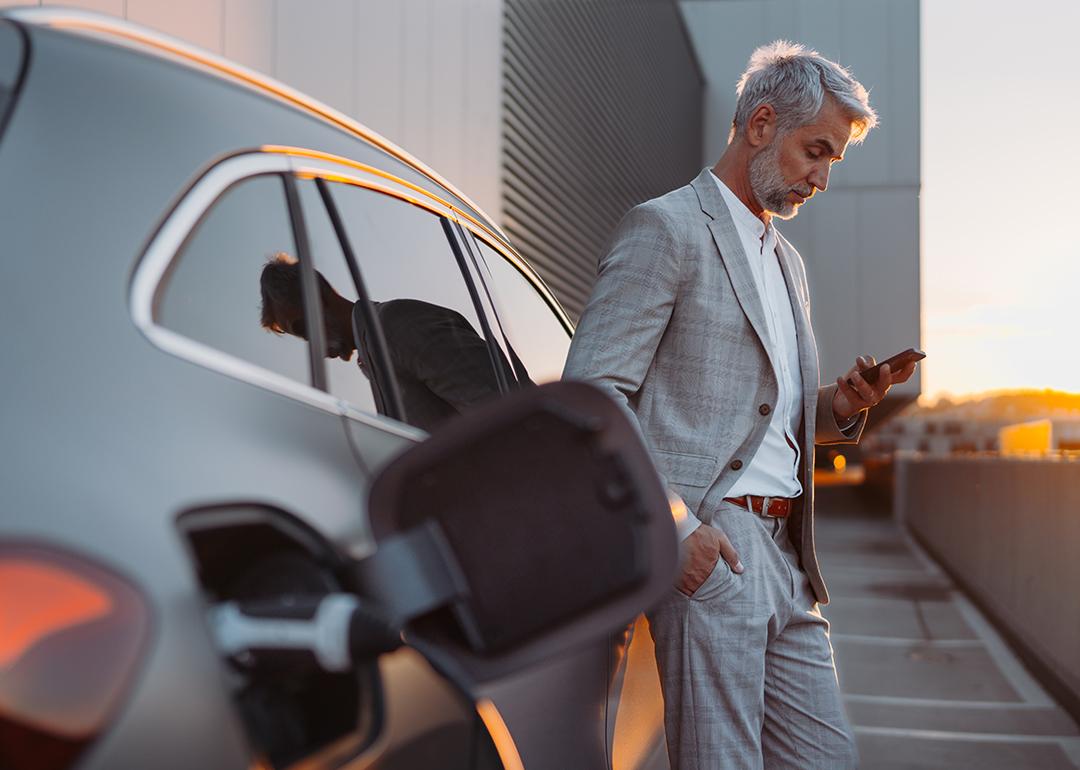 A man leaning on his electric car while using his smartphone.