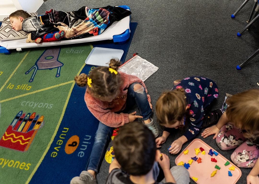 A group of young children during nap time at TLC for Tots daycare center in Nampa, Idaho. One child is sleeping while others are playing.