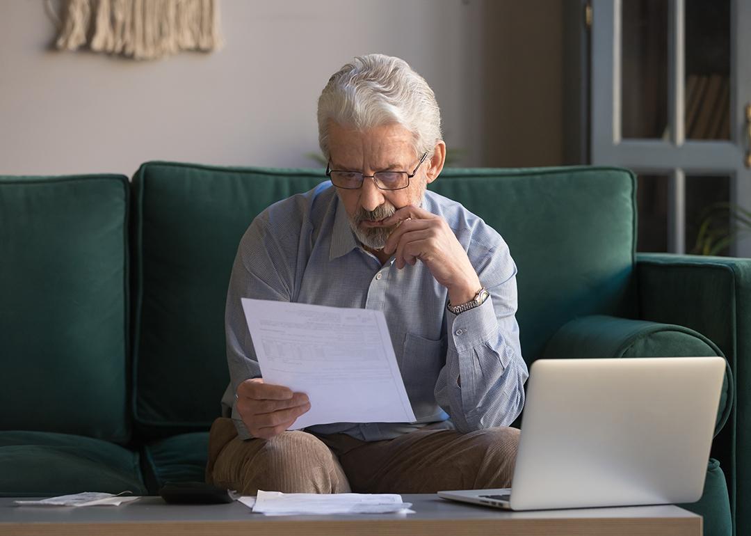 A senior man sitting on a couch intensely analyzing an expense bill.