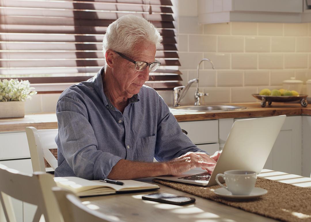 A senior man using a laptop in his kitchen.