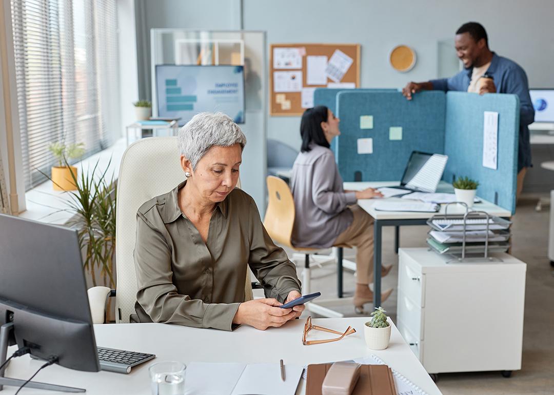 A senior businesswoman working at her desk in an open office setting.