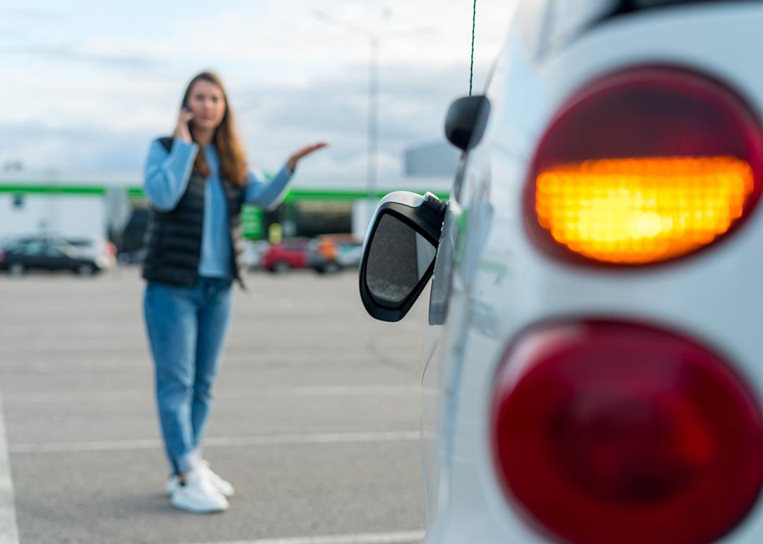 Woman talking on her phone while looking at her car's broken left side rear-view mirror.