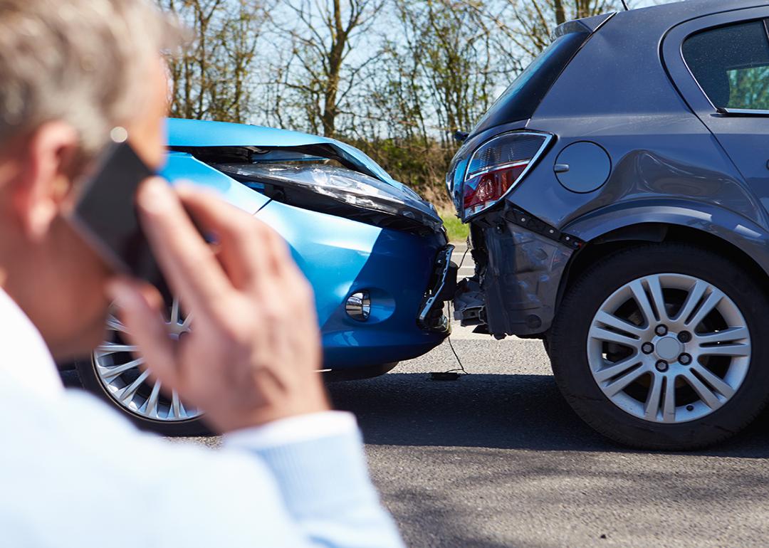 A car driver talks on the phone while looking at a rear-end collision.