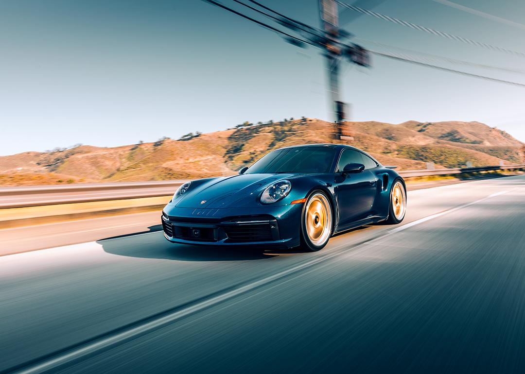 A black Porsche Turbo S driving on a highway with mountains in the background.