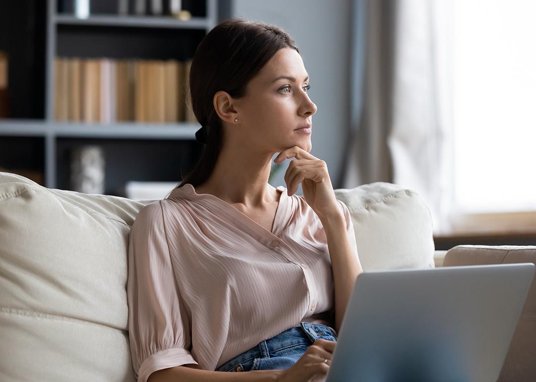 A young woman at home contemplating on couch while using laptop.