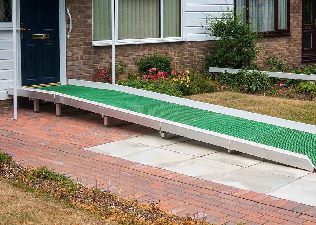 A wheelchair access ramp with green plastic surface installed at the door to a building that has a single step up to a black door.