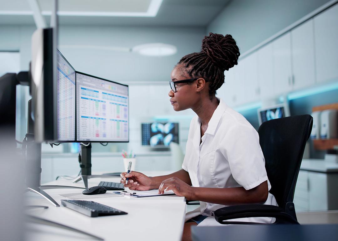A hospital staff looking at spreadsheets and billing codes using desktop with multiple monitors.