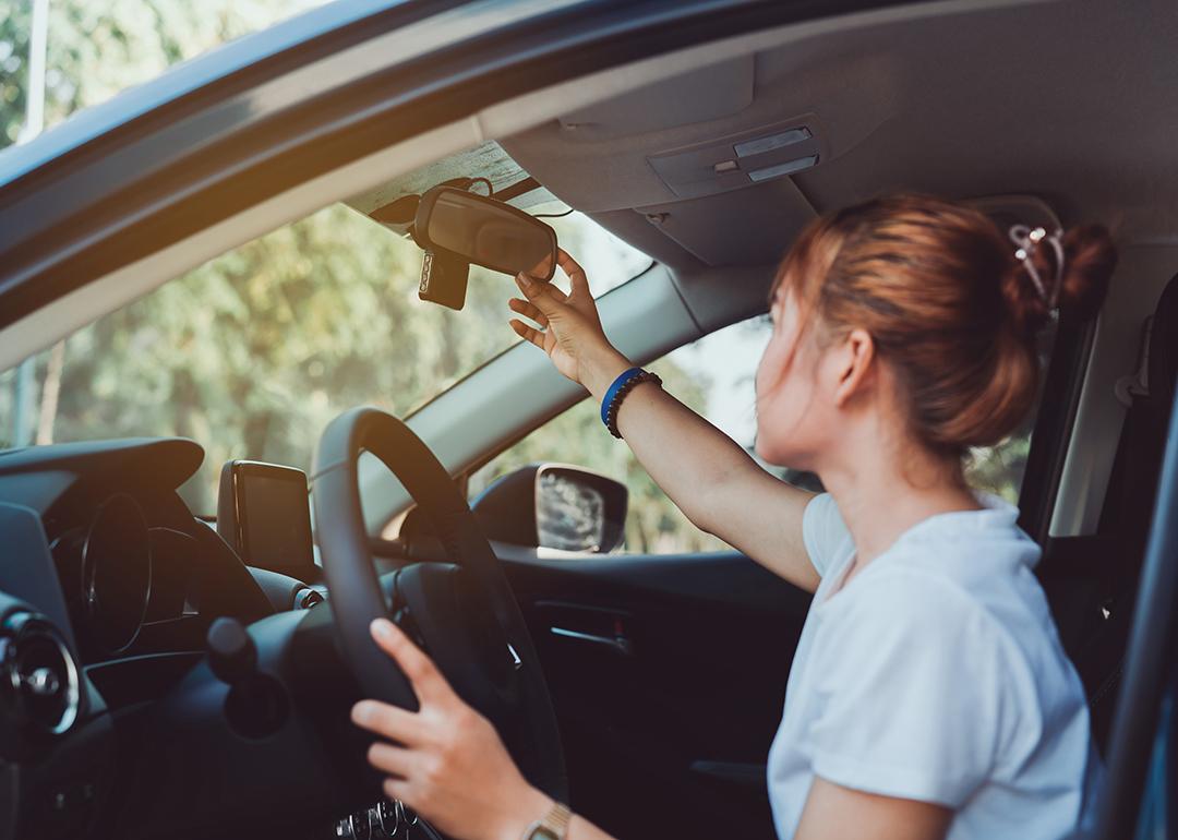 A woman adjusts her car's rearview mirror before driving.