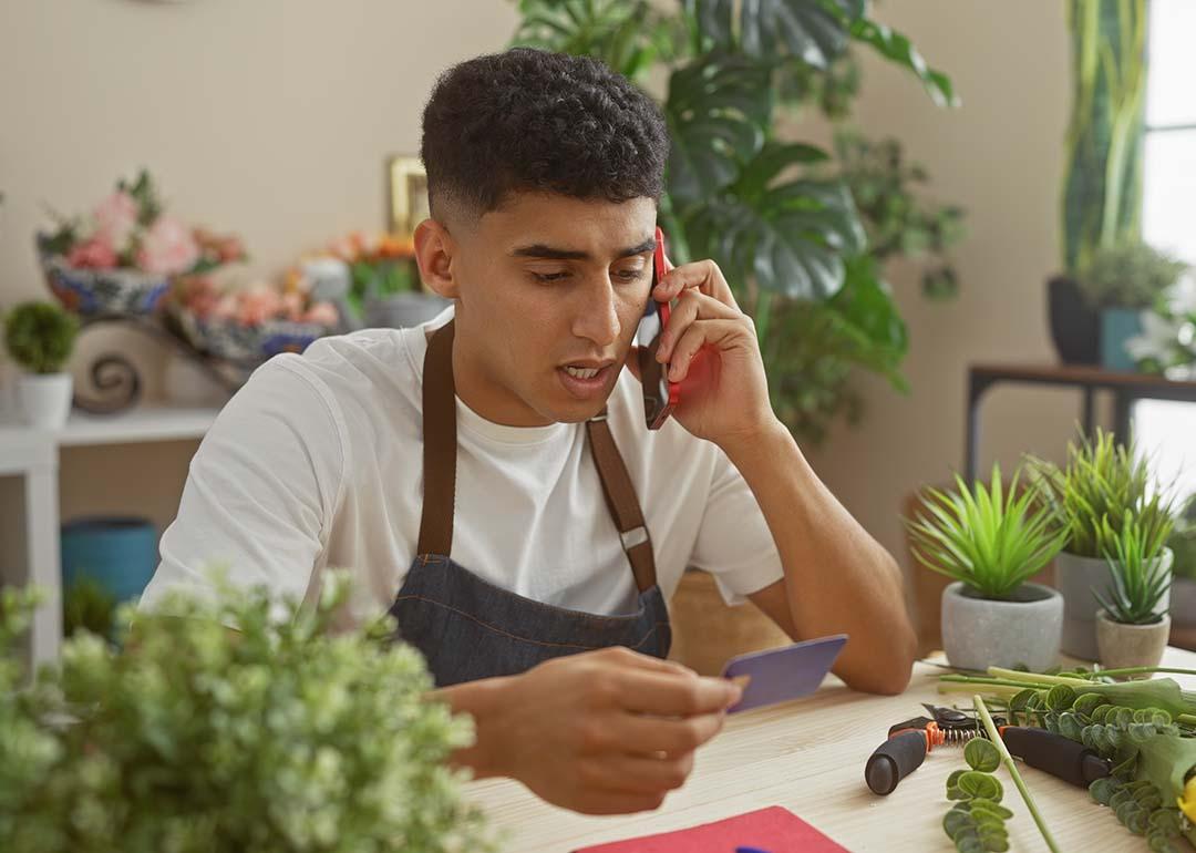 A flower shop business owner holding a credit card while talking on the phone.