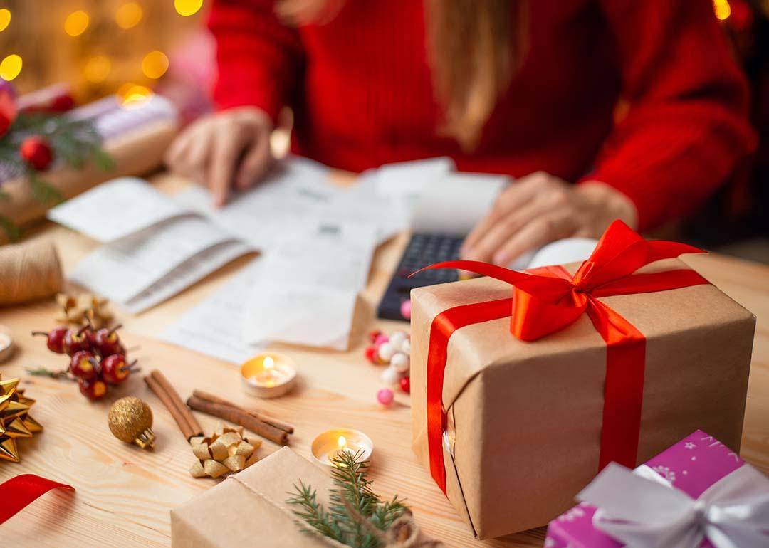 A woman calculates expenses on a table with holiday gifts and decorations.