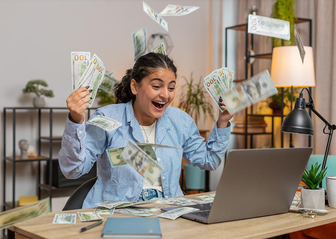 Young person throwing money and bills in the air in front of a computer; concept of getting rich quickly myth