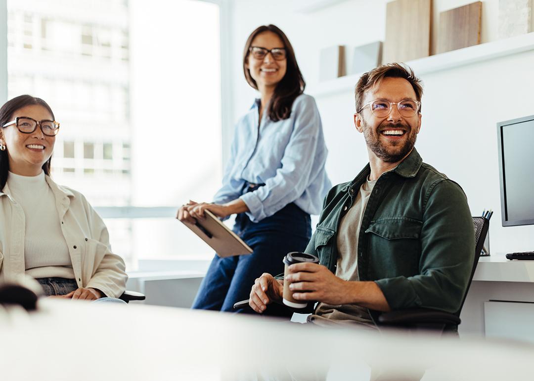 A group of three business people happily listens to a speaker during an office meeting.