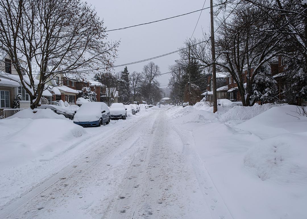 Unplowed snow accumulated on a residential street where rows of cars are parked.