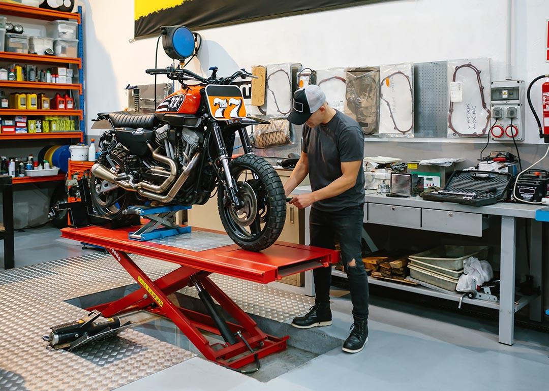 Unrecognizable mechanic man checking engine of custom motorcycle over platform.