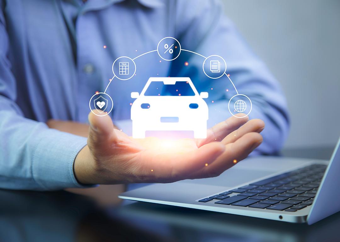 A car insurance agent using a laptop with graphics of car insurance concepts illustrated over his hand.
