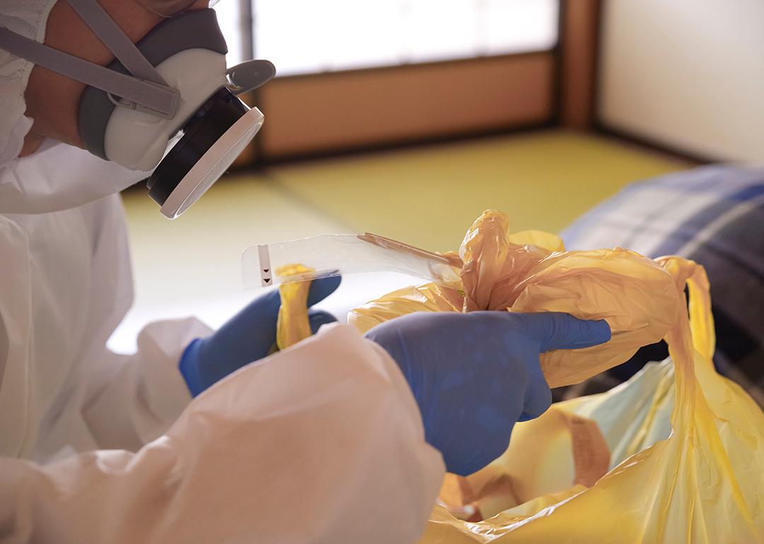 A crime scene cleanup worker in protective gear disposing garbage bags.