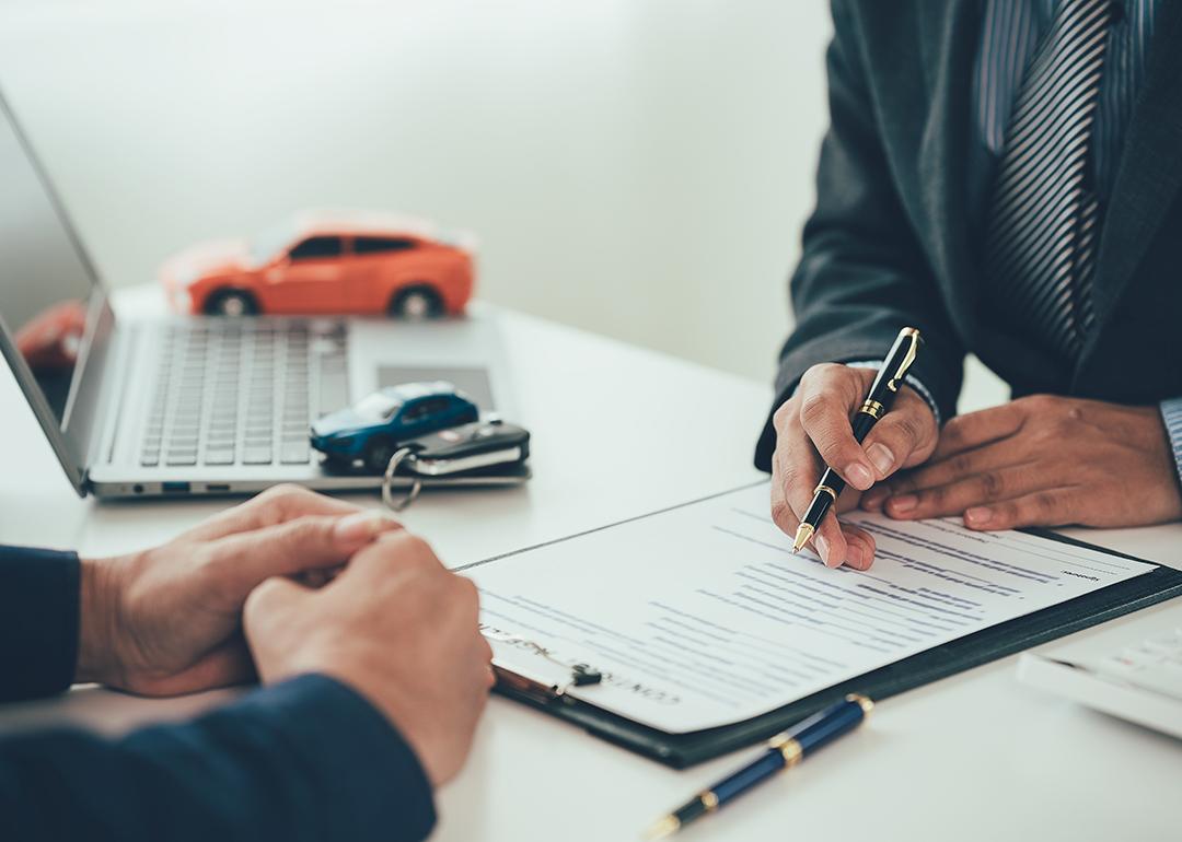 Figures of cars surround a table while a car salesperson transacts with a customer.