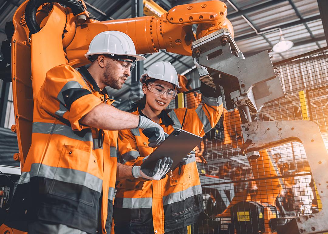 Two members of an engineering team looking at programming in a tablet inside their automated manufacturing factory.