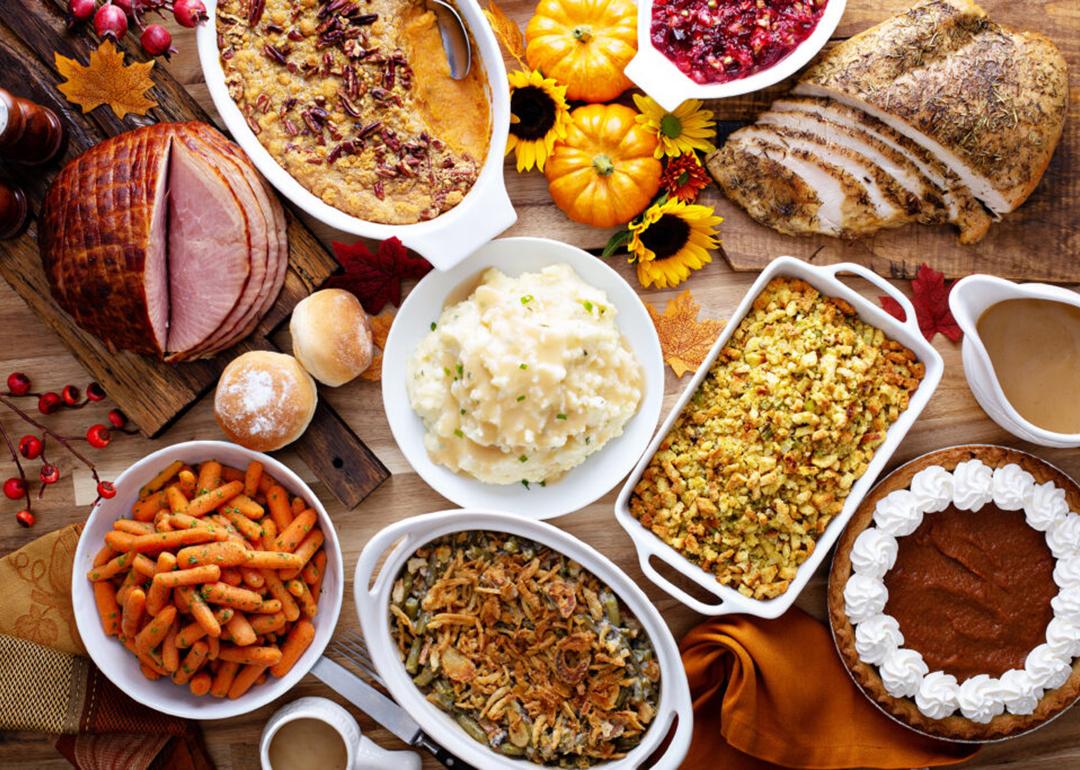 A table full of traditional holiday and Thanksgiving dishes such as mashed potato, ham, turkey, stuffing, and pumpkin pie.