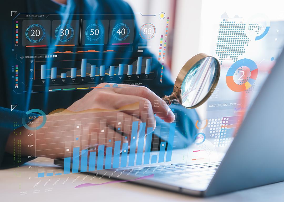 Person holding a magnifying glass close to a laptop screen, illustrated with data charts and graphics.