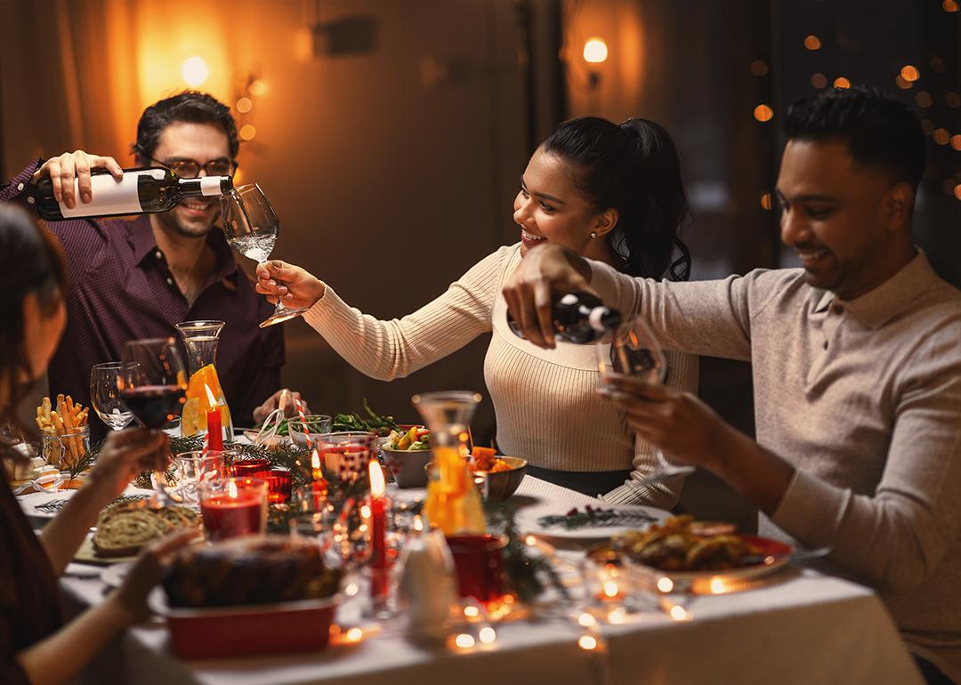 A group of happy friends pouring wine in their glasses during Christmas dinner.