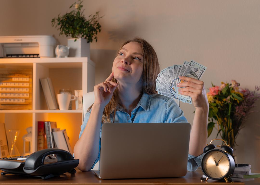 A female manager holding cash daydreaming in an office.