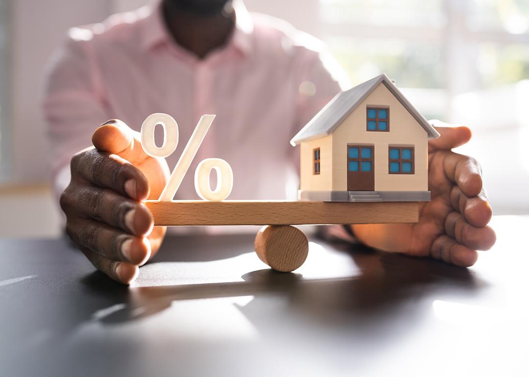 A person balancing figures of a percentage and a small house.