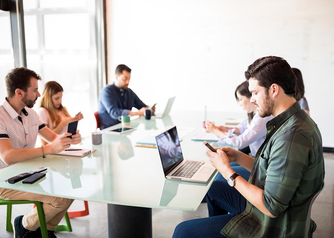 A business team in a meeting room but each member is using their phone.