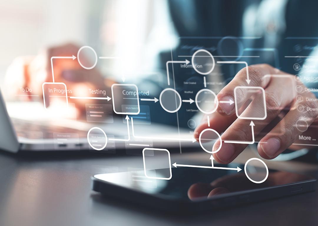Person using a laptop and phone illustrated with automated business workflow chart graphics.