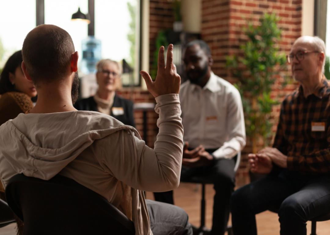 A group circle meeting with one man holding up his hand.