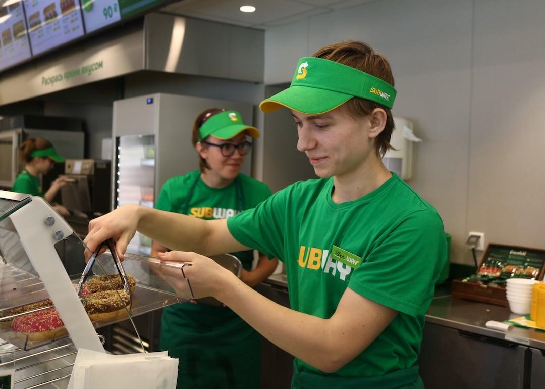 Subway worker grabbing a donut from display container.