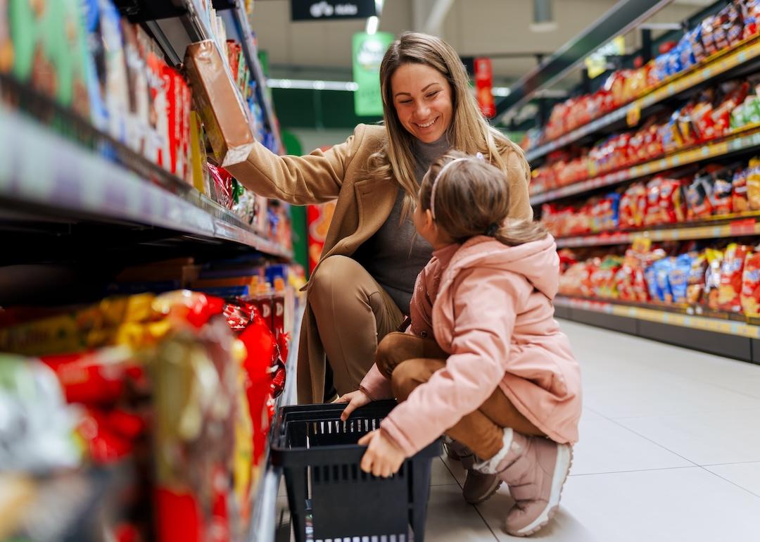A woman and little girl shopping for snacks in a grocery aisle.