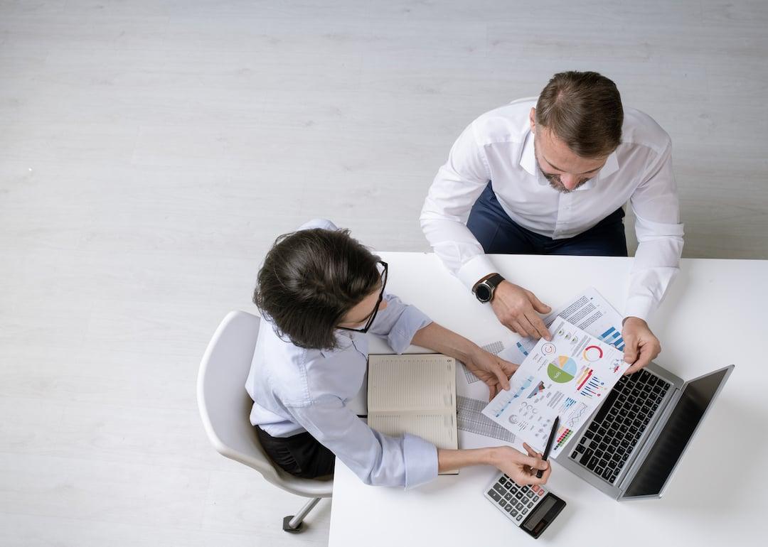 Overhead view of two successful colleagues discussing financial papers with diagrams and charts at a work meeting.