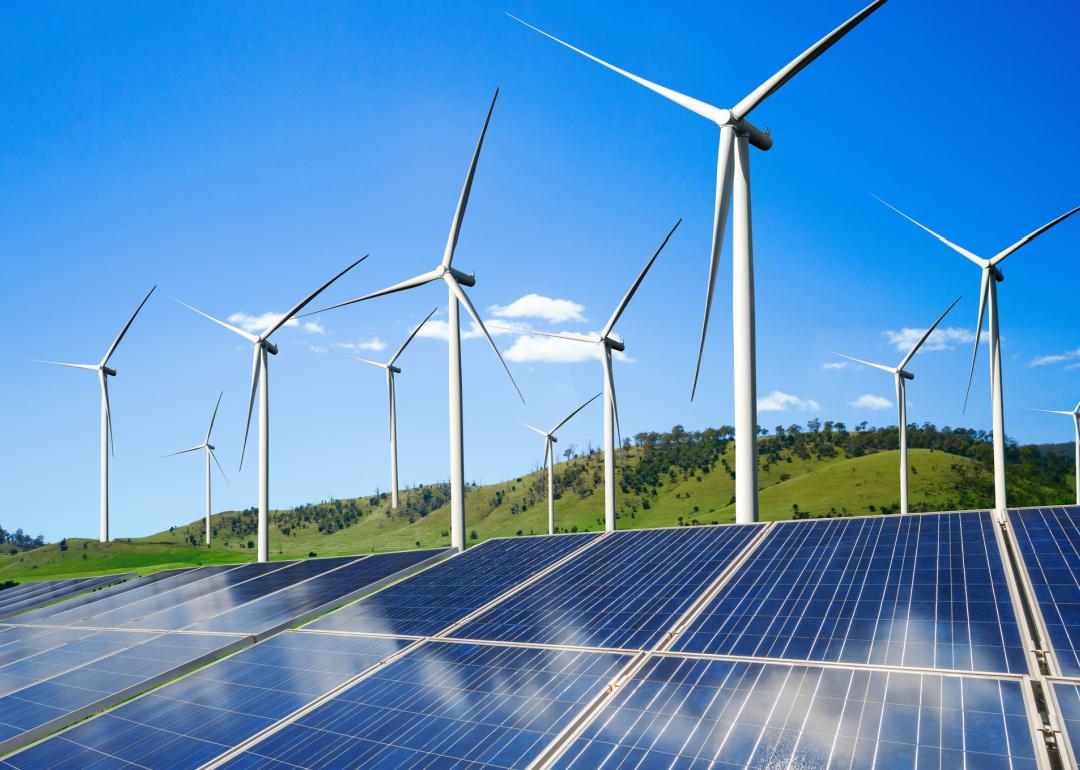 Solar panels and wind turbines in grassy field with blue sky