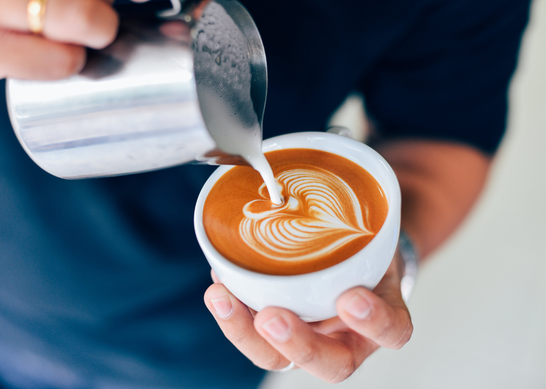 Barista pouring milk in coffee drink.
