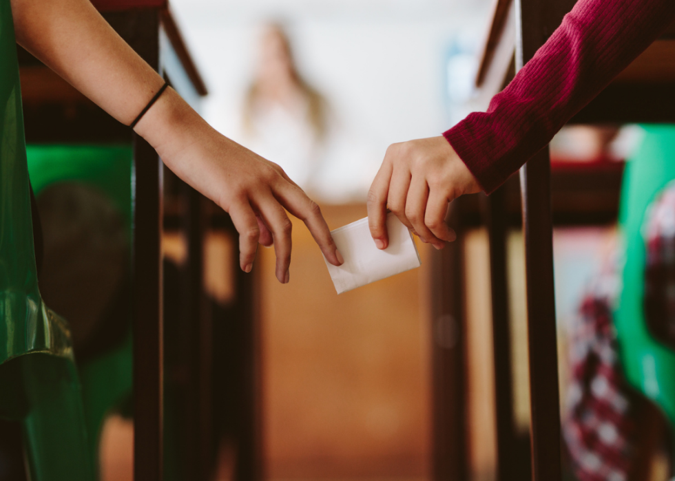 Hands of two students passing a note in class