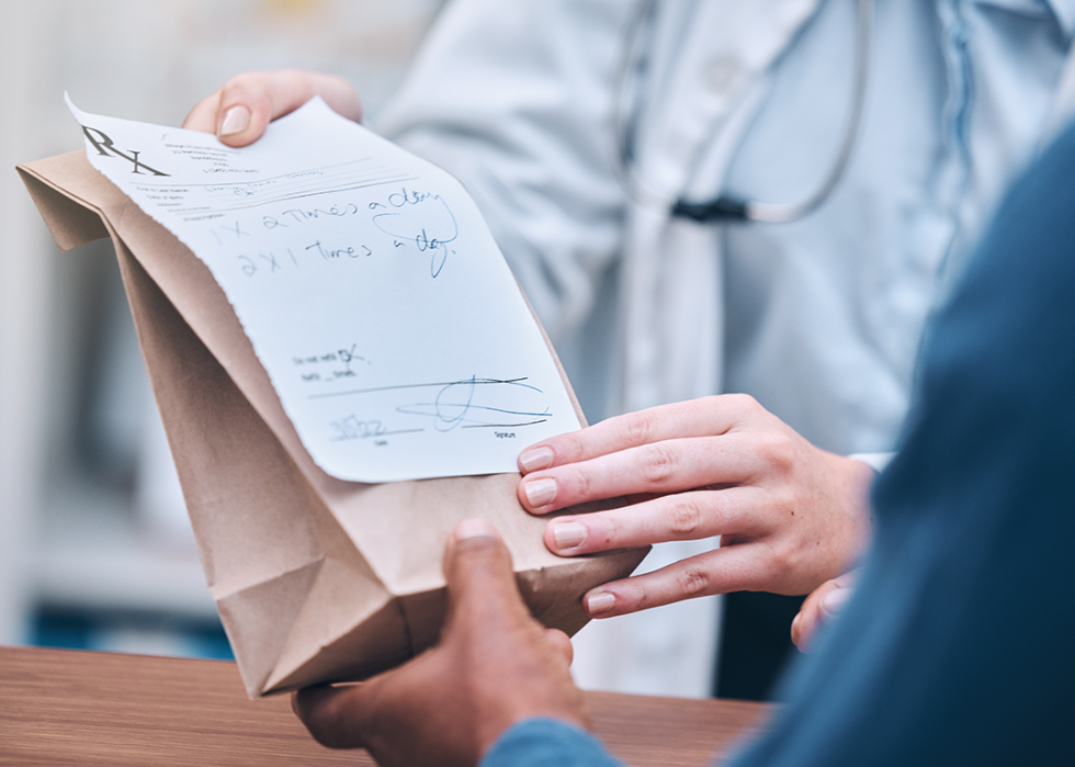 Pharmacist handing prescription bag to customer.