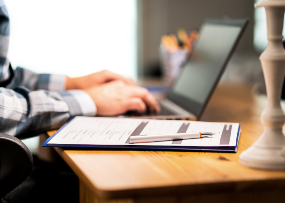 Person with documents and pen typing on laptop