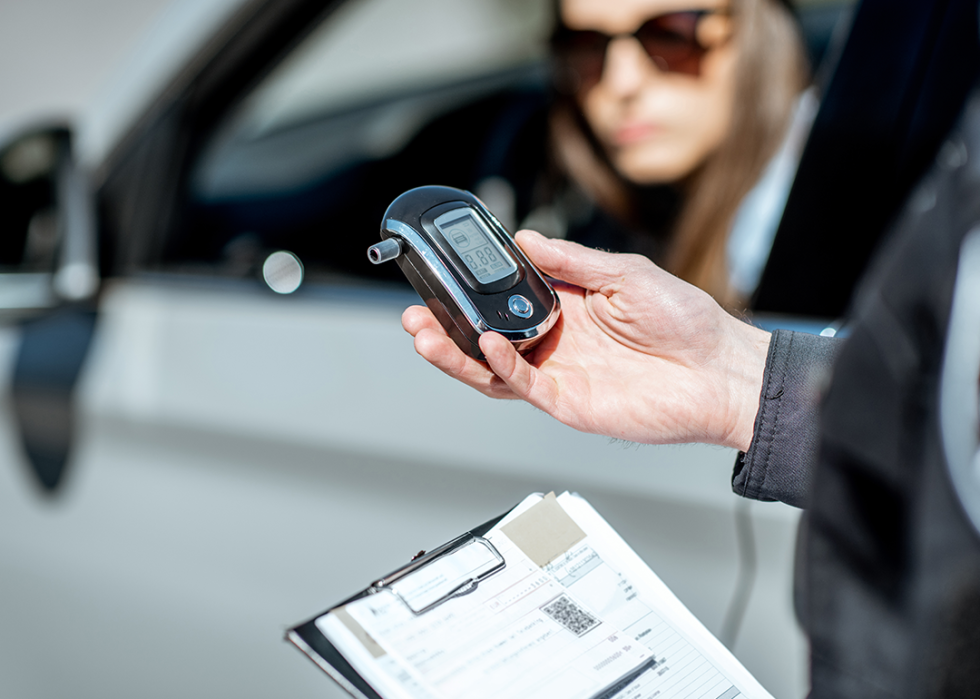 Police officer holding device for checking alcohol intoxication beside a stopped vehicle with a driver at the wheel.