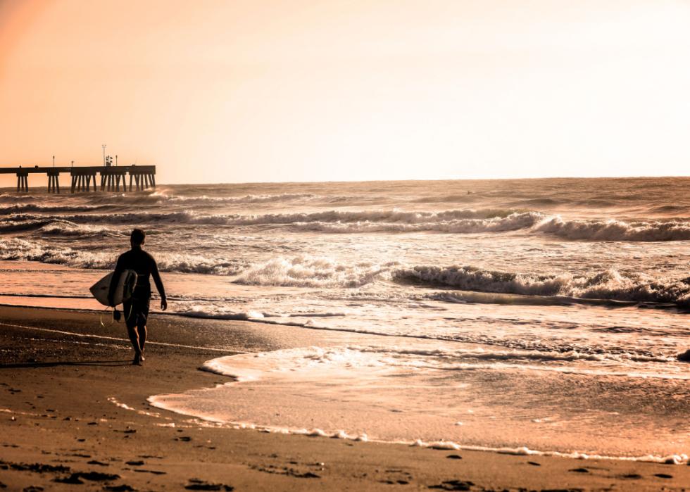 Man with surfboard on beach with sunset.