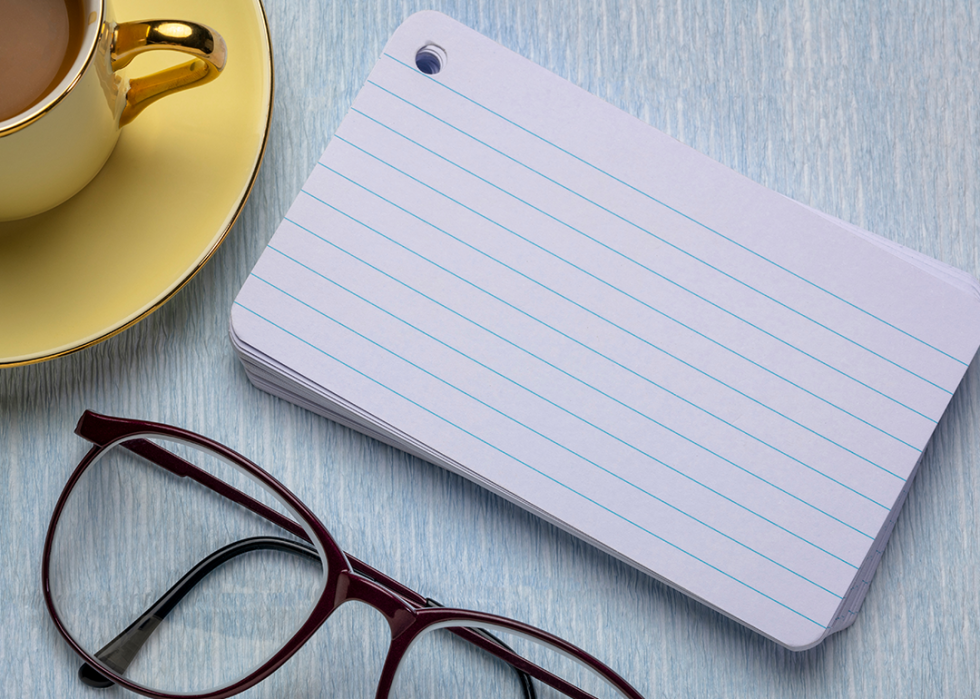 A mug next to blank index cards and glasses on a table.