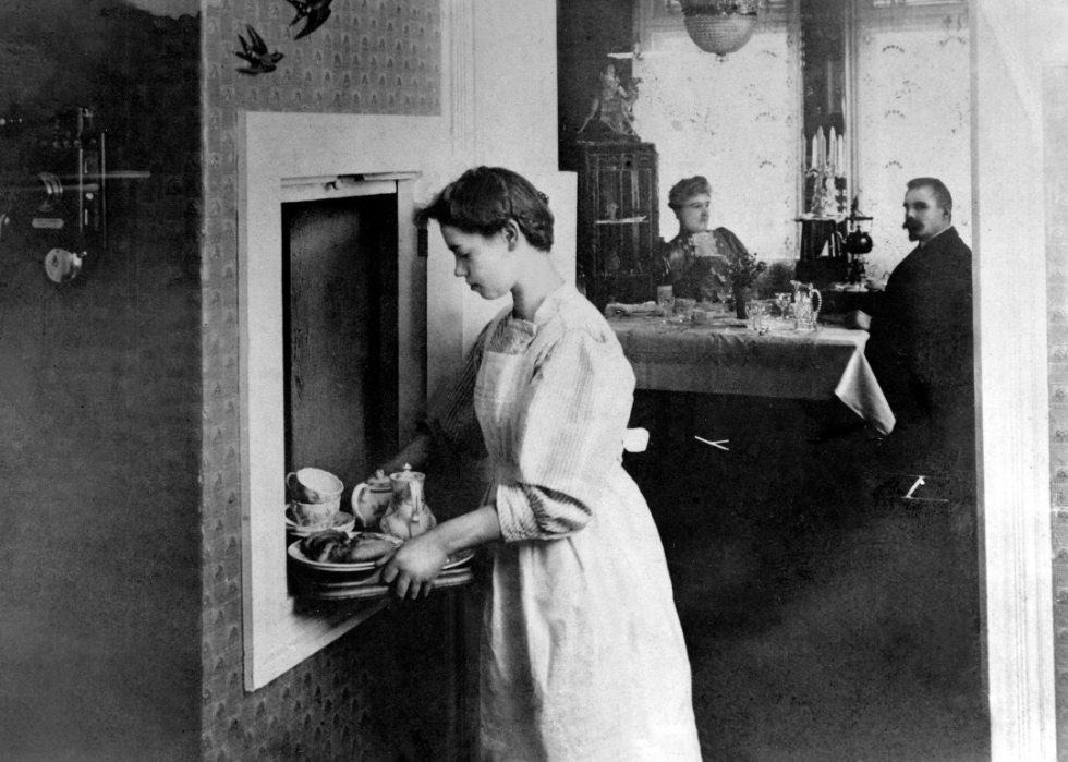 A server puts dinner plates into a dumbwaiter.
