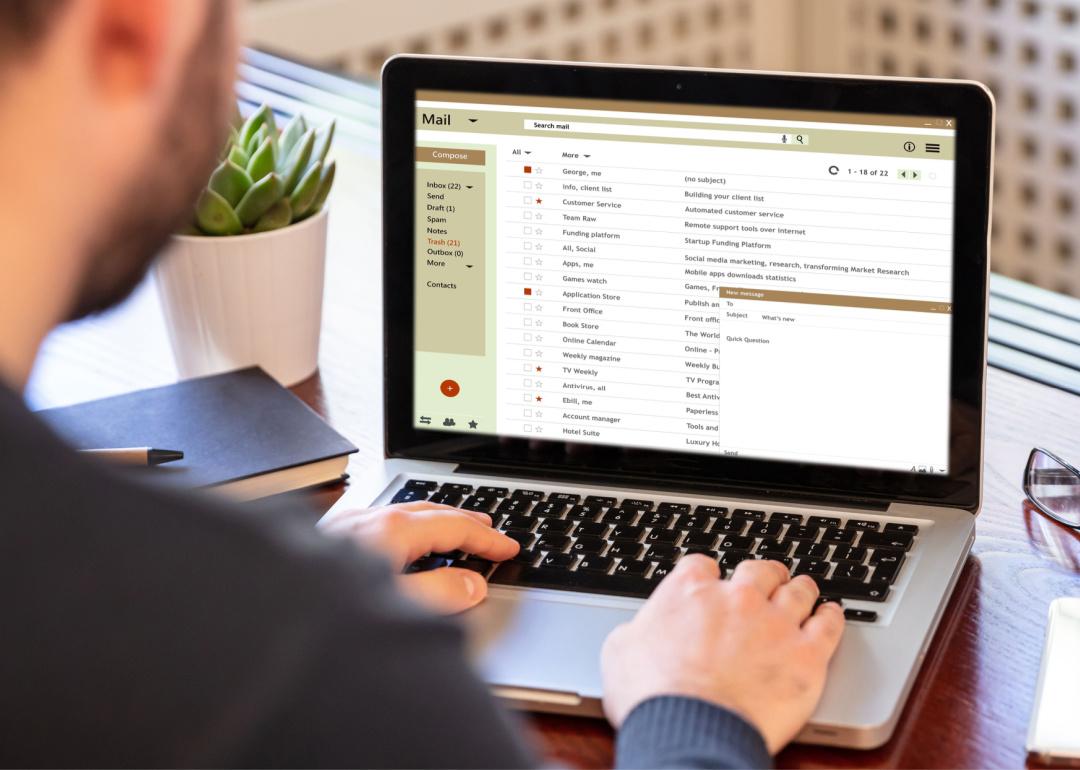 Man working at desk with email inbox on laptop screen.