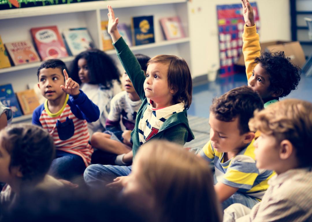 Elementary school students sitting in group with hands raised.