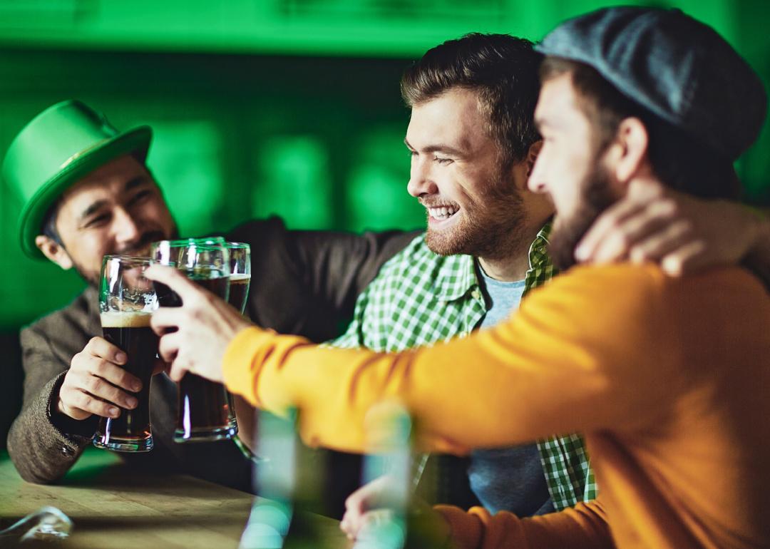 Three male friends toasting with beer in bar during St. Patrick's Day.