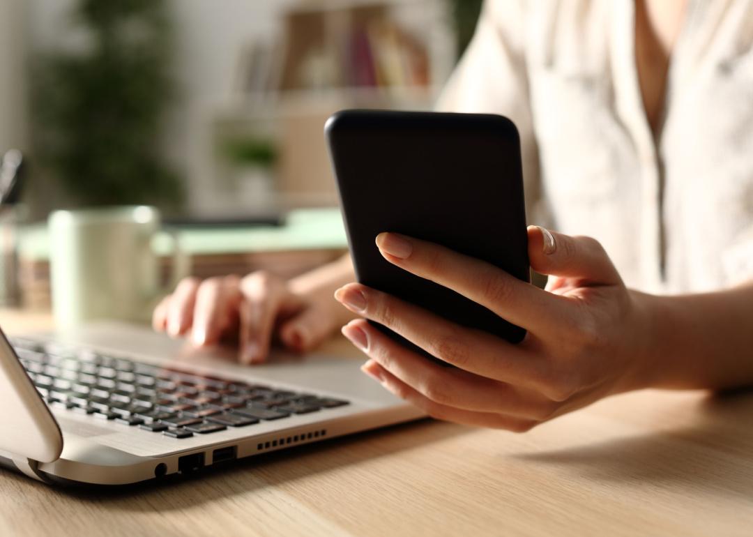 Person holding phone with laptop open.