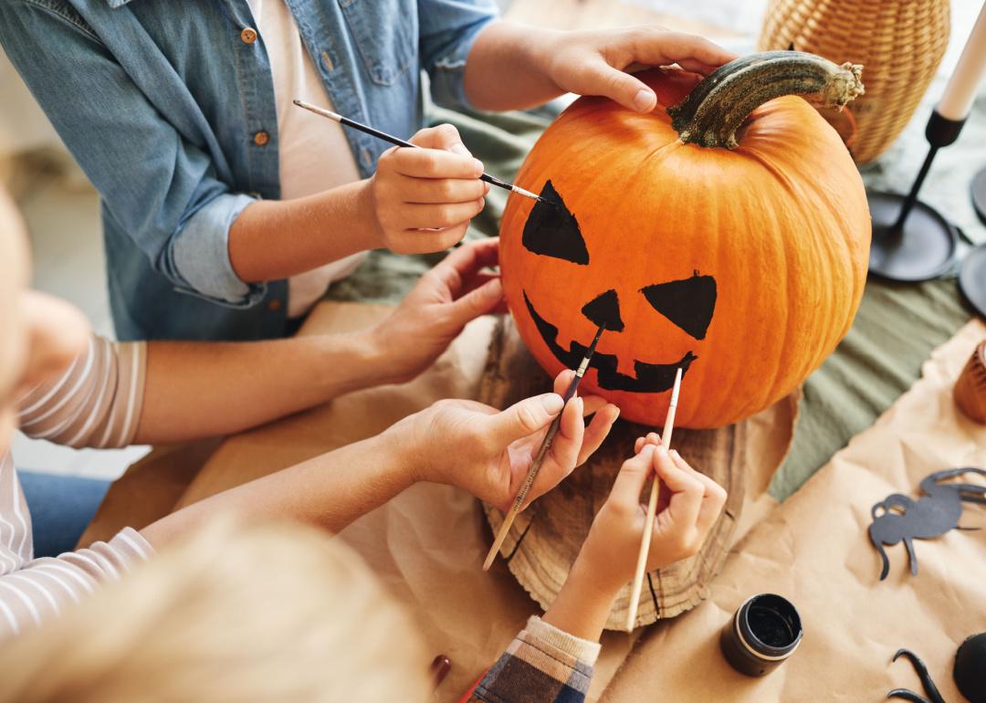 Close up of hands painting a face on a pumpkin.