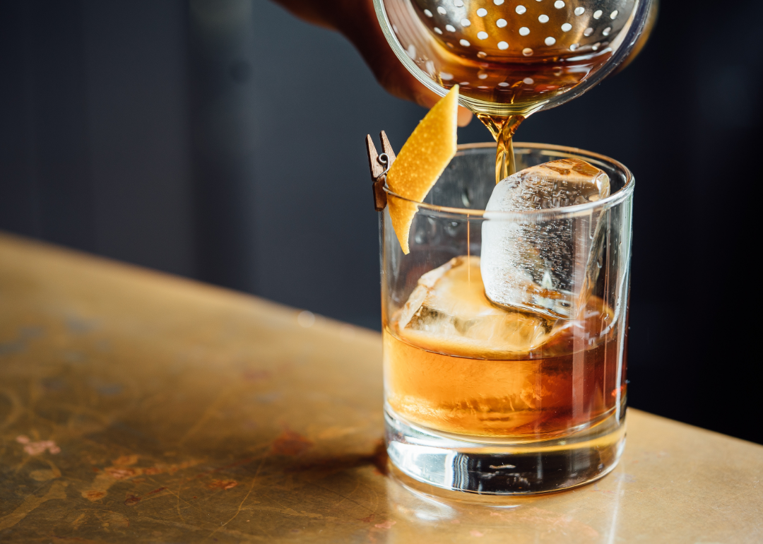 Close up pouring cocktail into glass on bar.