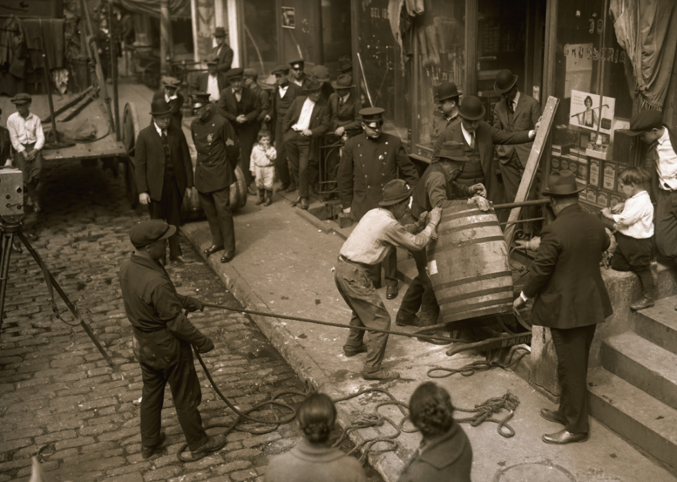 Police and crowd watching men remove wine barrel