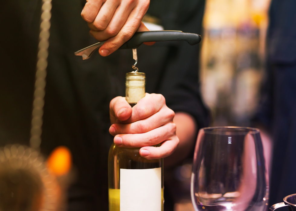 Close up hands opening wine bottle with corkscrew